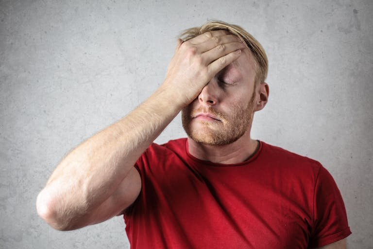 A frustrated man in a red shirt holds his head in doubt.