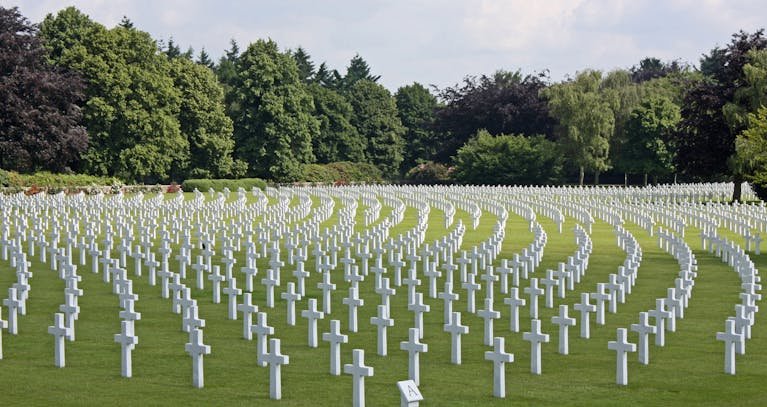 A serene military cemetery with rows of white crosses surrounded by lush greenery.